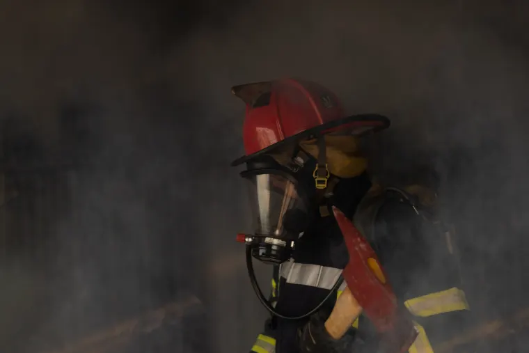 Imagen de un bombero equipado con casco rojo y hacha en un entorno con humo, representando el entrenamiento para brigadas de protección civil y el logo de MASI